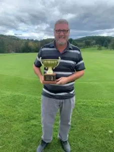 Man holding golf trophy on a golf course.