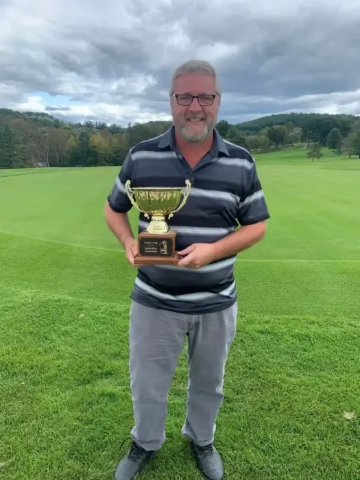 Man holding golf trophy on a golf course.