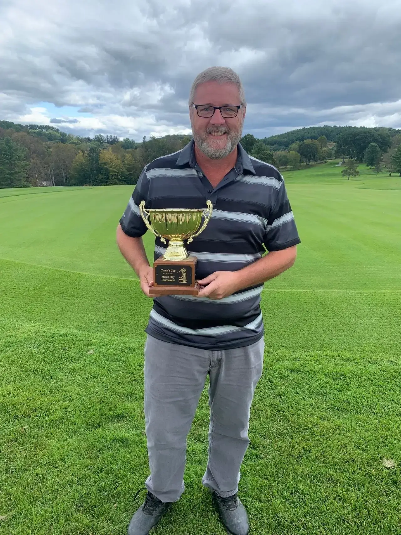 Man holding golf trophy on a golf course.